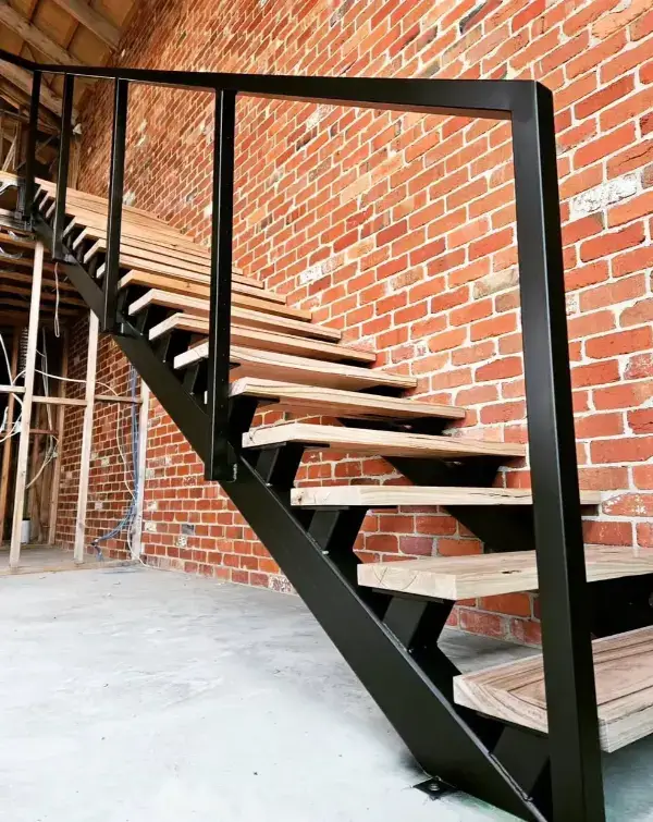 A custom steel staircase with black steel and wooden treads installed in front of a brick wall