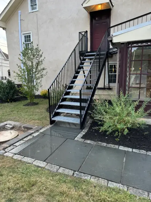 An outdoor steel staircase with black steel and grating treads installed on the exterior wall of a residence