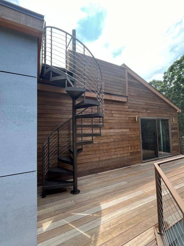 Black metal spiral staircase installed on the deck of a home with wood siding